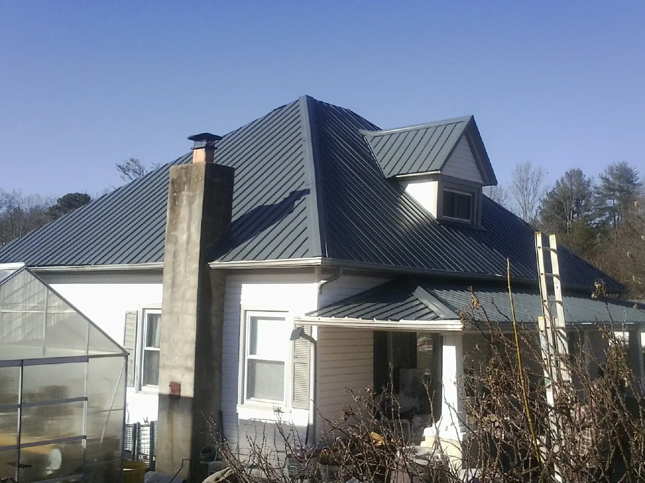 Dark blue standing seam metal roof on a white farmhouse with dormer — Slate & Tile Roof Repair by Roofing Brothers in Browns Summit