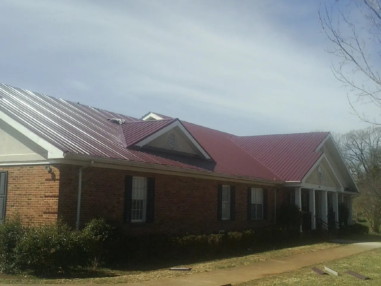 Red metal roof with gabled entries on a long brick building, from a Hail Damage Roof Repair job in Browns Summit