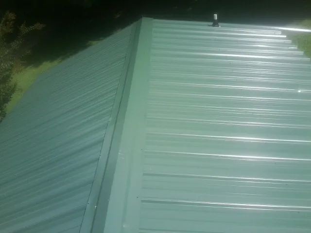 New green metal panels meeting at the ridge of a roof — Flat Roof Repair work by our crew in Browns Summit
