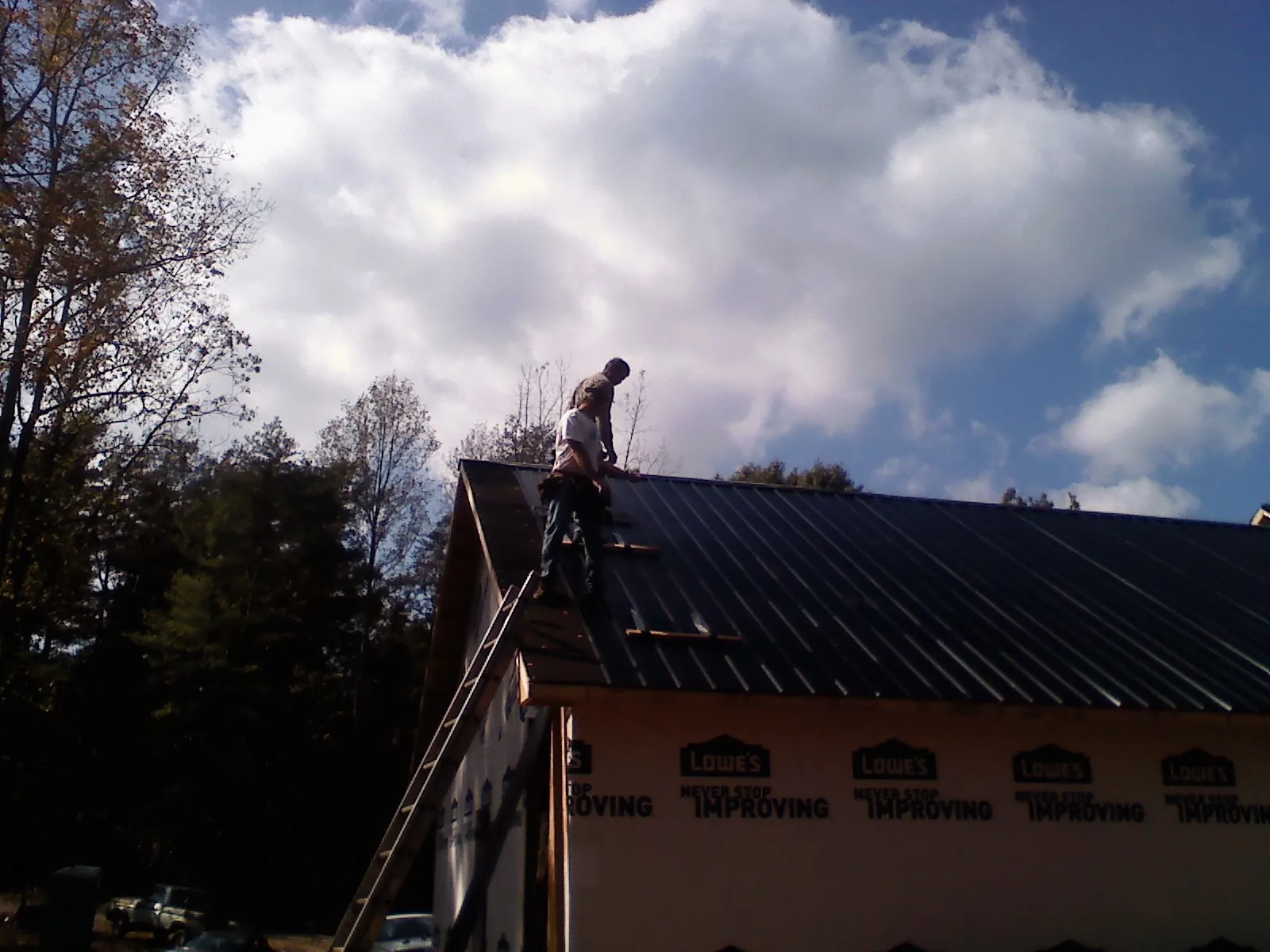 Roofer fastening dark metal panels high against a cloudy sky, from a Roof Inspection job in Browns Summit